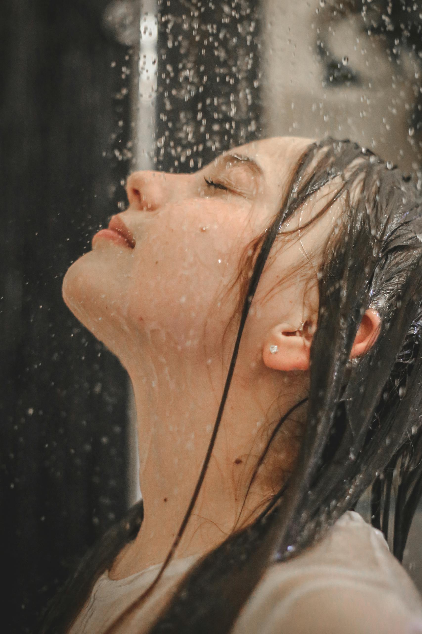 Graceful side profile of a woman embracing the rain shower indoors.